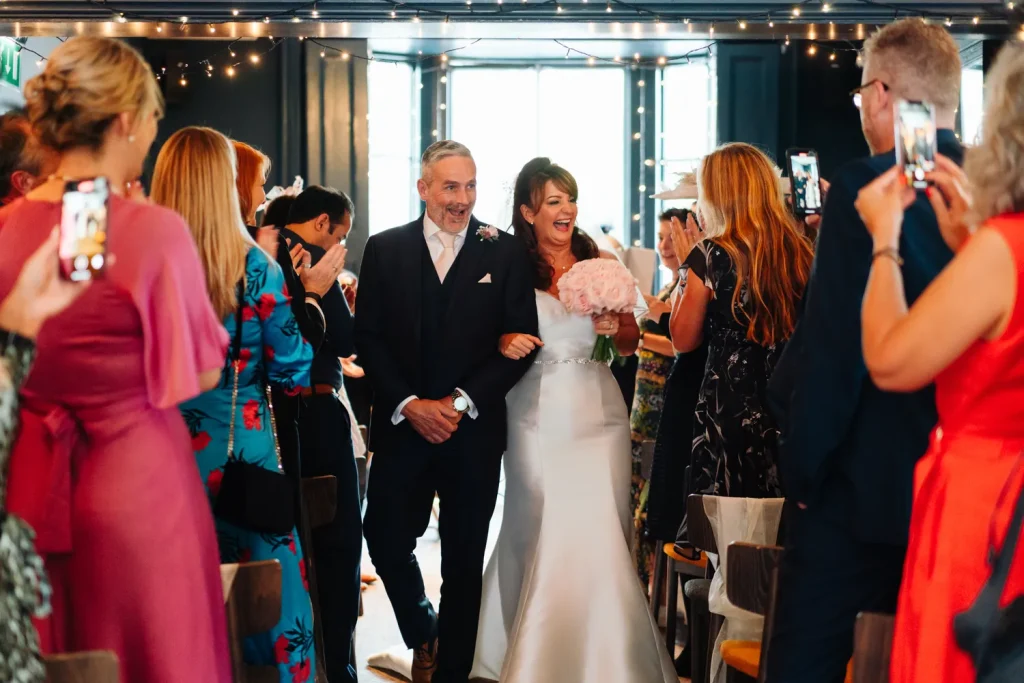 Guests following the newlyweds through Norwich toward Plantation Garden for the wedding photoshoot, an umbrella visible in the background