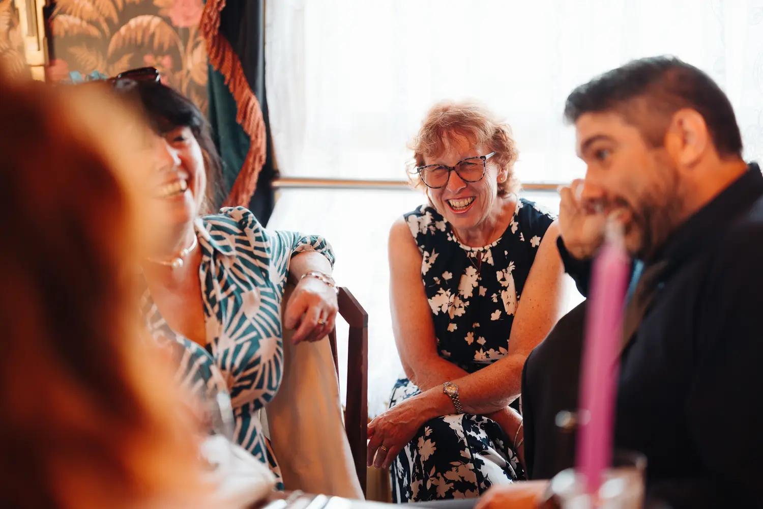 Older female wedding guest laughing warmly at the dining table during the reception at The Cosy Club Norwich, surrounded by other guests in the vibrant venue