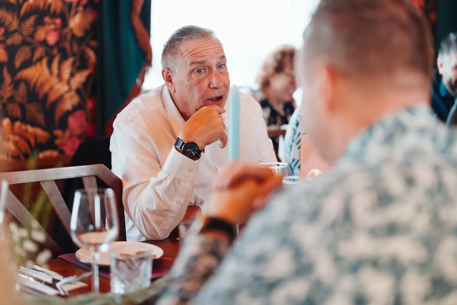 Older male wedding guest in conversation at the dinner table during the reception at The Cosy Club Norwich, listening intently over wine glasses and candles