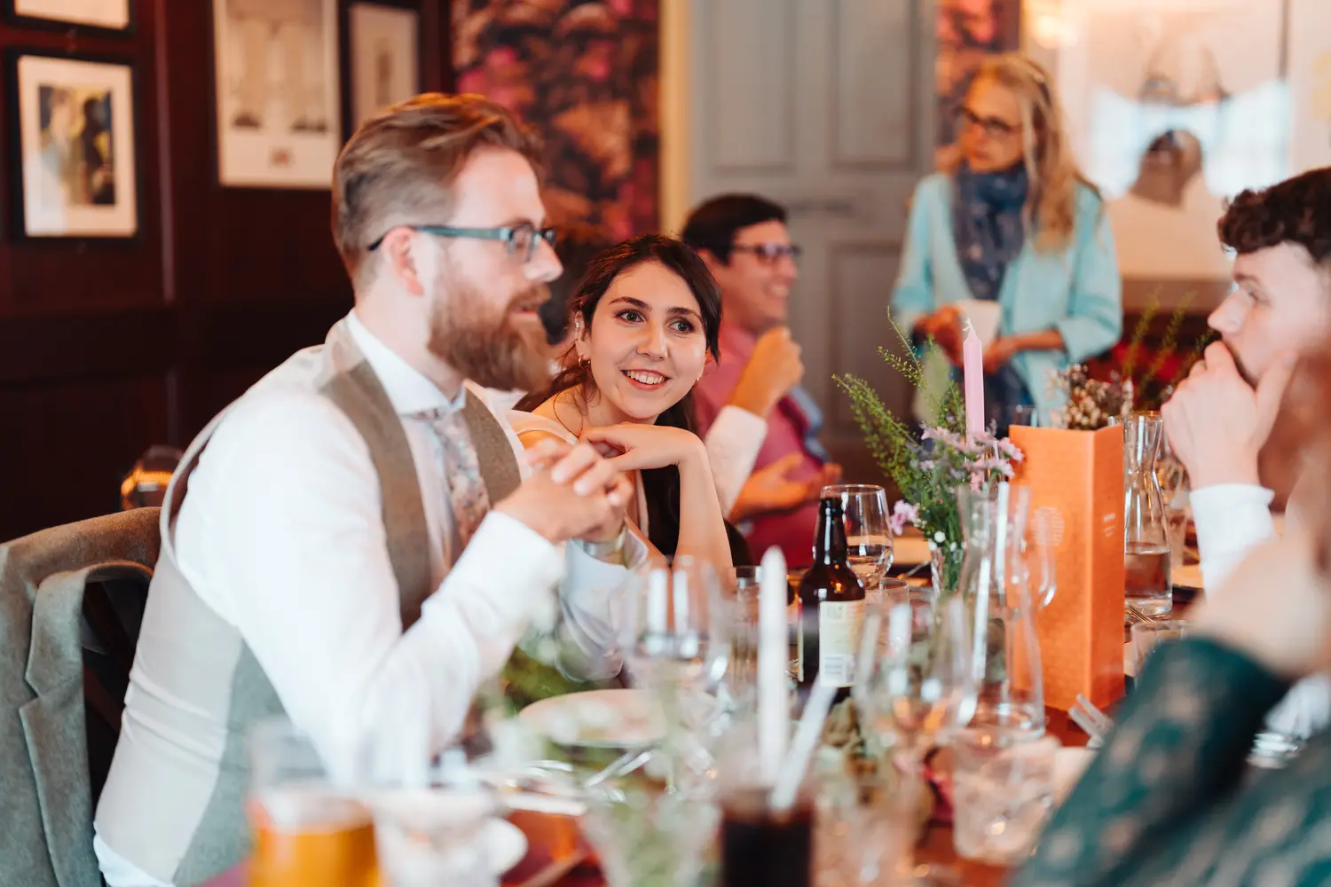James and Sarah chatting and smiling at the top table during their wedding reception dinner at The Cosy Club Norwich, colourful drinks and table decorations around them