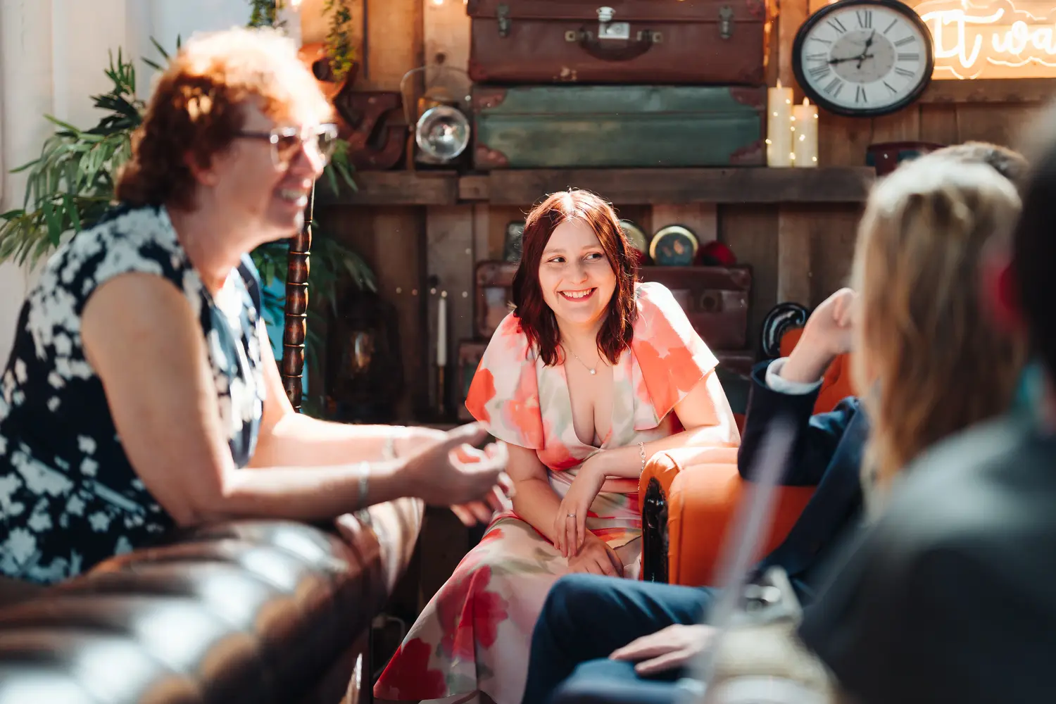 Female wedding guest smiling and chatting inside the quirky Flint Rooms venue in Norwich, vintage suitcases and clock in the background