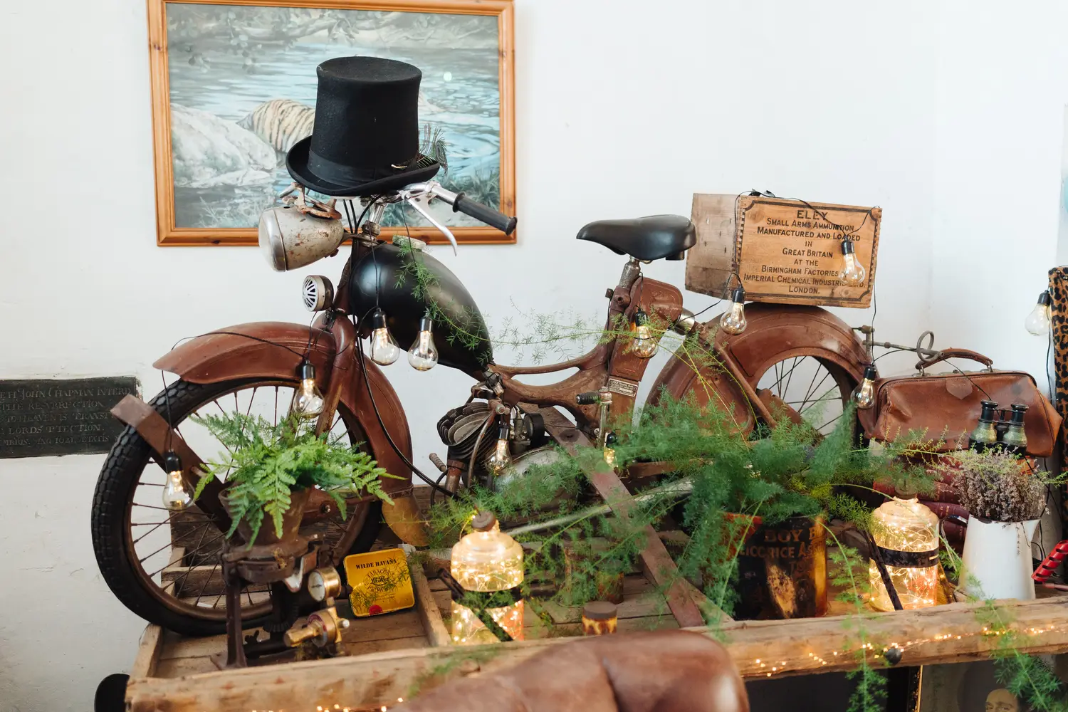 Vintage motorcycle decorated with a top hat, fairy lights, and ferns — a quirky detail inside The Flint Rooms wedding venue in Norwich