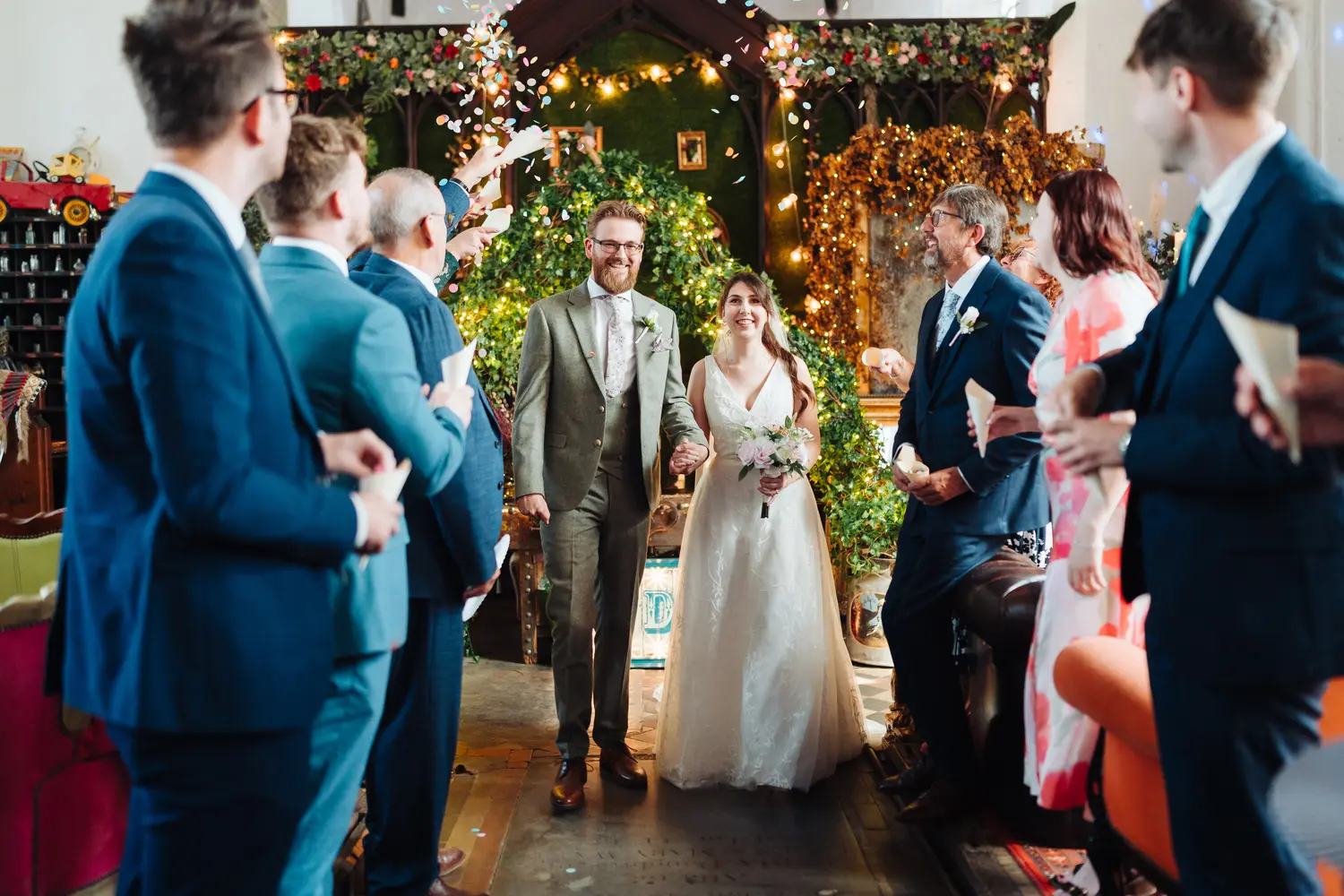Sarah and James walking back up the aisle hand in hand at The Flint Rooms Norwich as guests prepare to throw colourful confetti in celebration