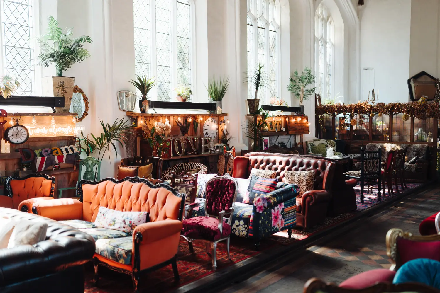 Interior of The Flint Rooms wedding venue in Norwich showing eclectic mismatched vintage sofas, fairy lights, and colourful decor with tall gothic windows