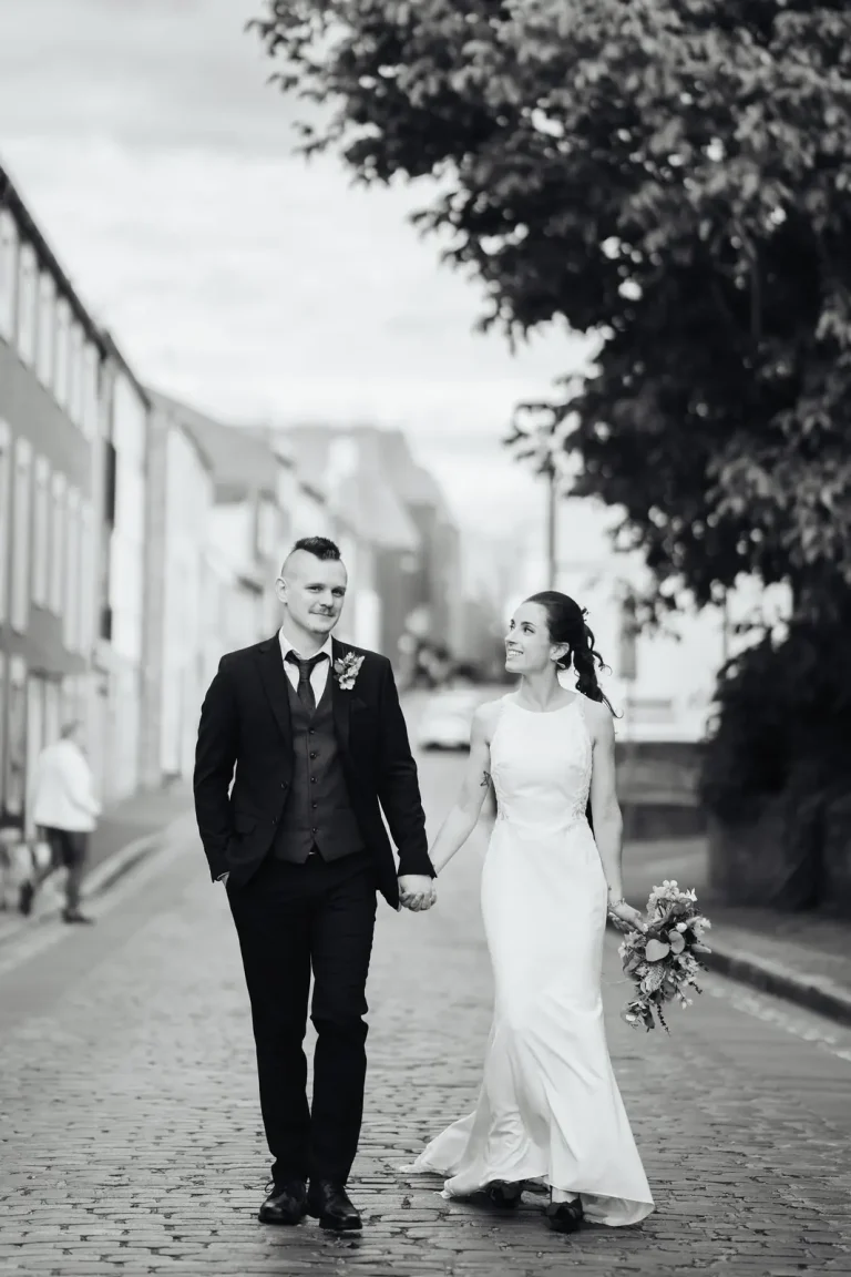 Bride and groom walking hand in hand along cobbled streets in black and white — urban city wedding portrait