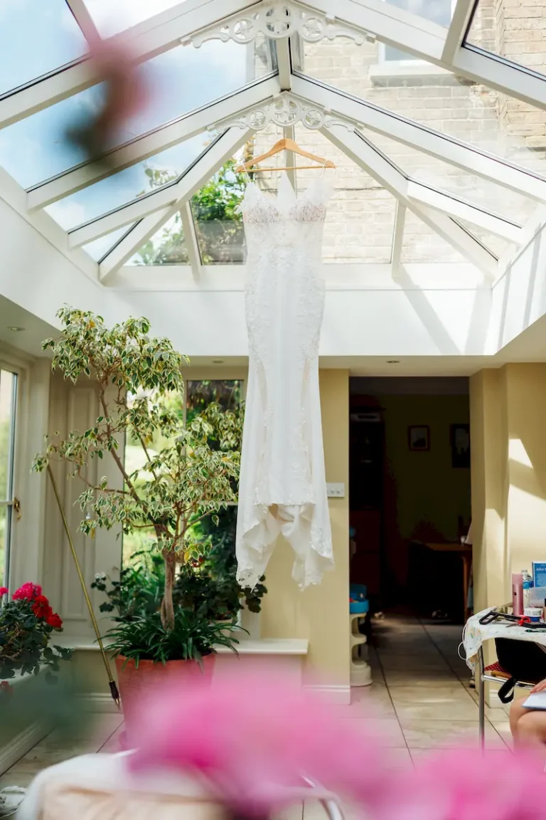 Antonia’s lace wedding dress hanging in the glass roof of the conservatory during morning prep