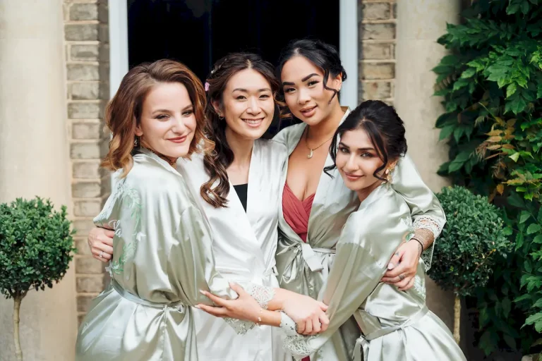 Antonia hugging her bridesmaids in sage satin robes outside on the morning of her wedding