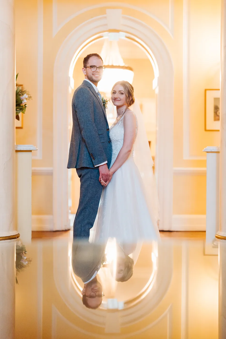 A beaming married couple posing in a exquisite light-filled archway at a wedding venue.